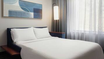 A hotel room with a large bed, a nightstand, a modern lamp, a painting, and sheer curtains.