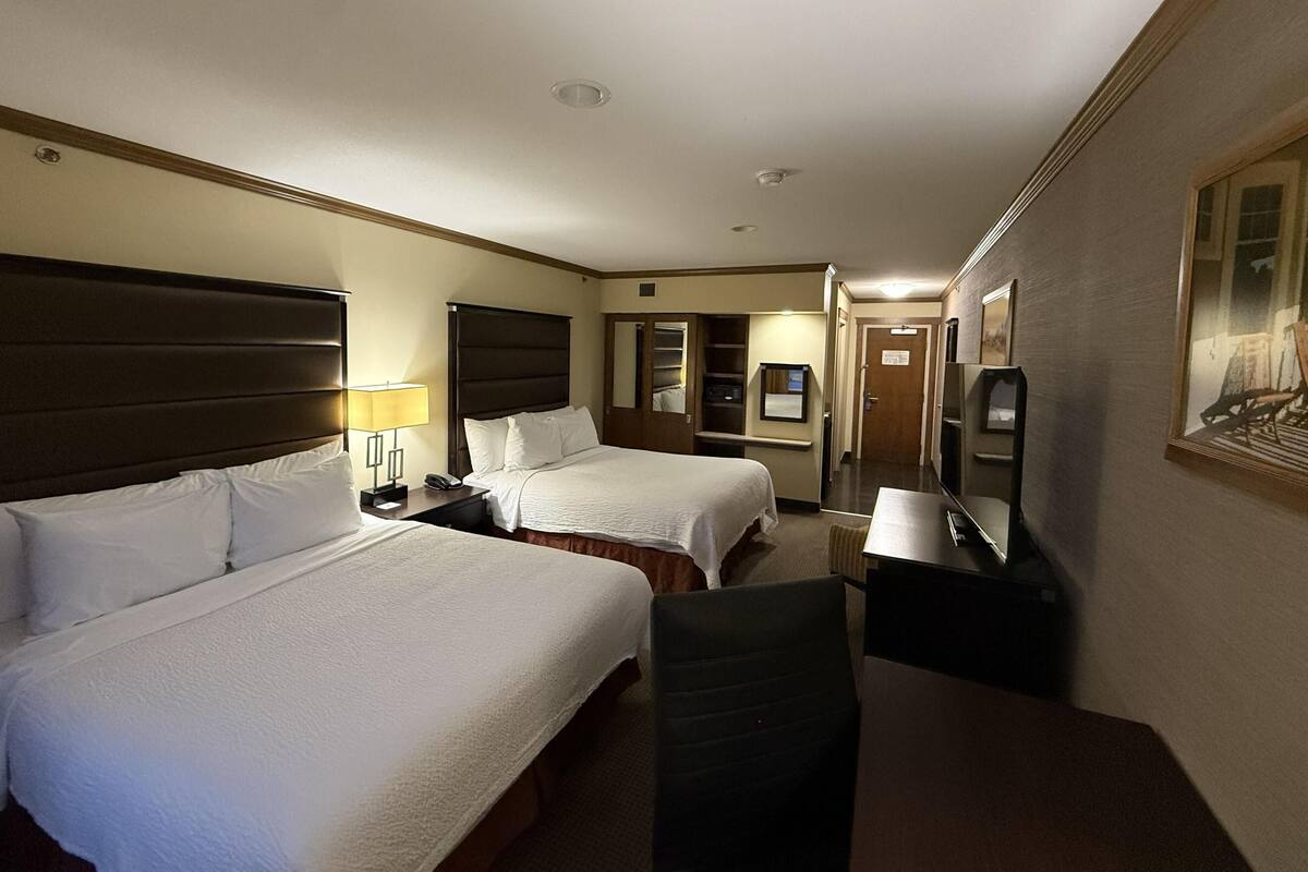 A hotel room with two beds, a desk, a chair, a TV, and a door leading to a bathroom.