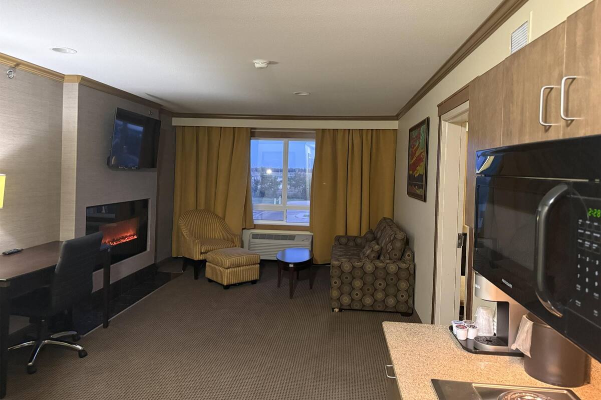 A hotel room with a flat-screen TV, a fireplace, a sofa, a dining table, and a kitchenette with a microwave.