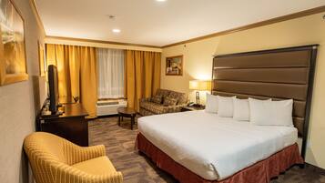 A hotel room with a large bed, a sofa, a desk with a lamp, and a television.