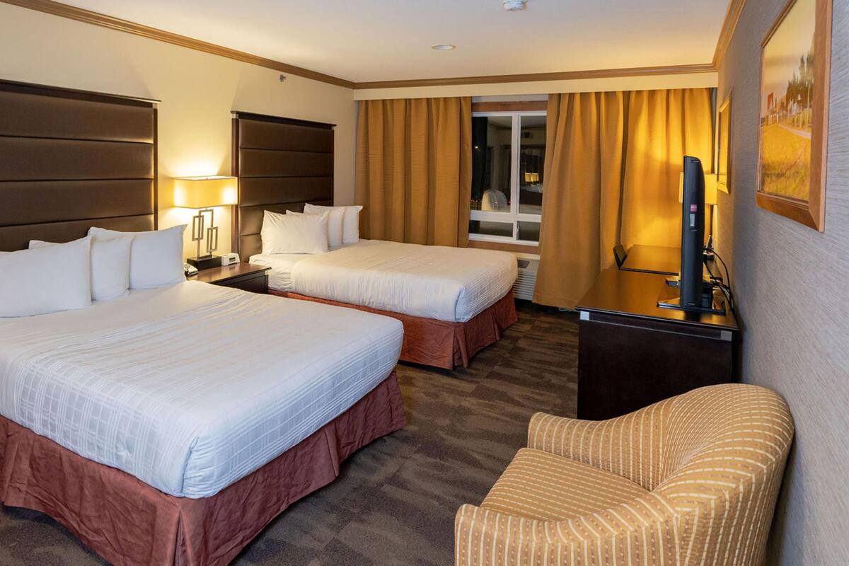 A hotel room with two beds, a desk, a chair, and a television.