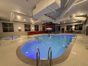 Une piscine intérieure avec un toboggan rouge, une eau claire et un sol carrelé.