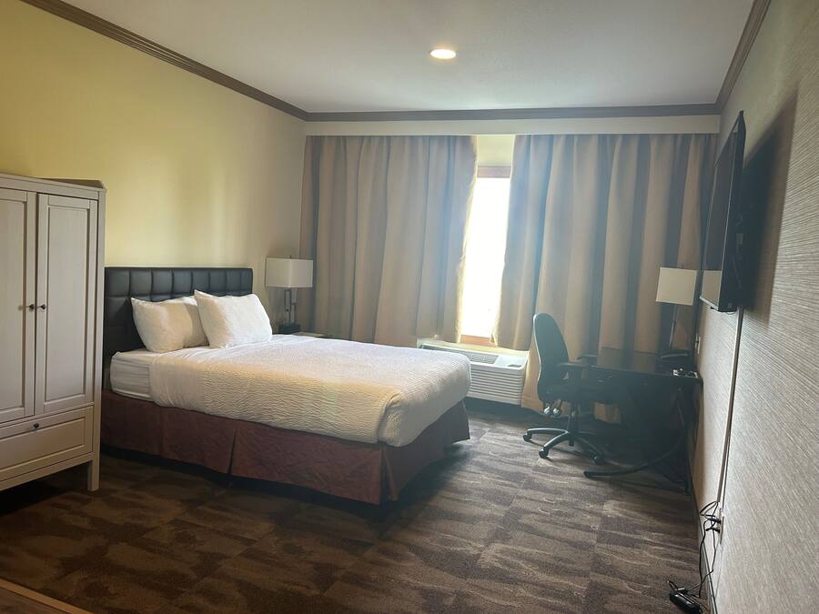 A hotel room with a bed, a desk, a chair, a wardrobe, and a television.