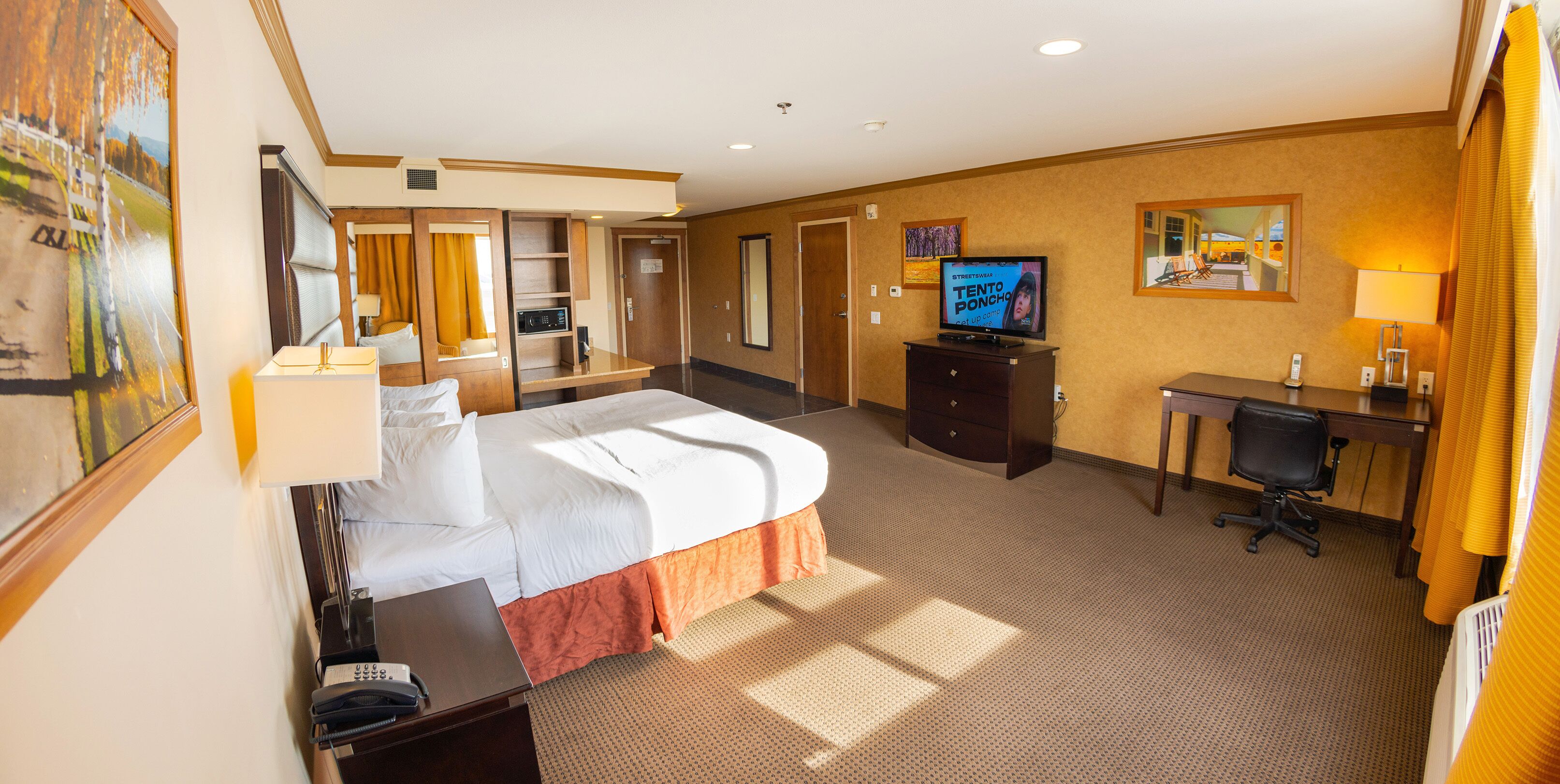 Quarto de hotel com cama, escrivaninha, televisão e espelho.