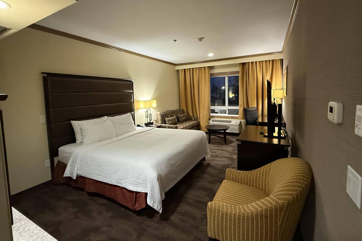 A hotel room with a bed, a sofa, a chair, a desk, and a window with curtains.