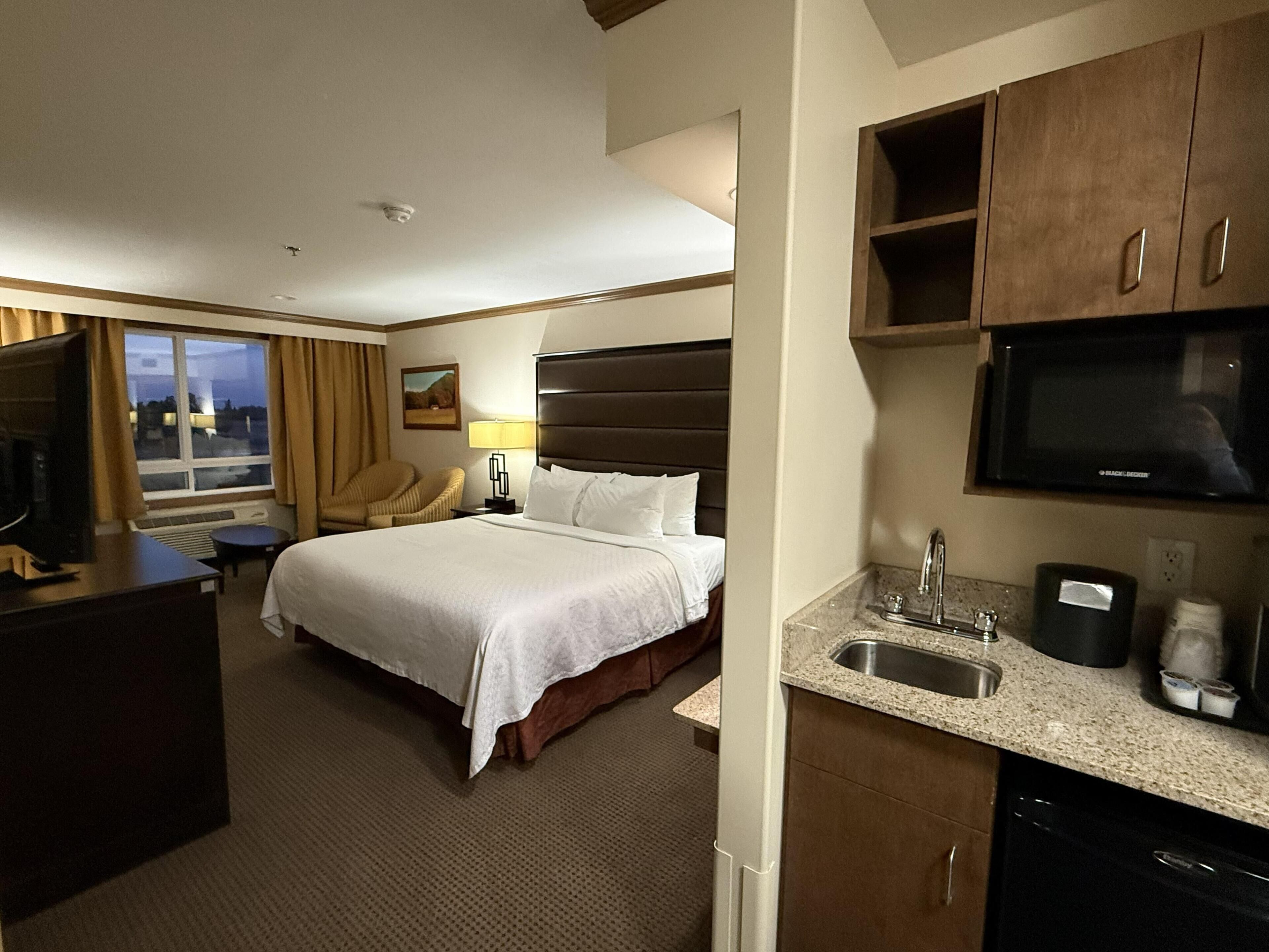 Habitación de hotel con cama, escritorio, silla, televisión, lavamanos y ventana.