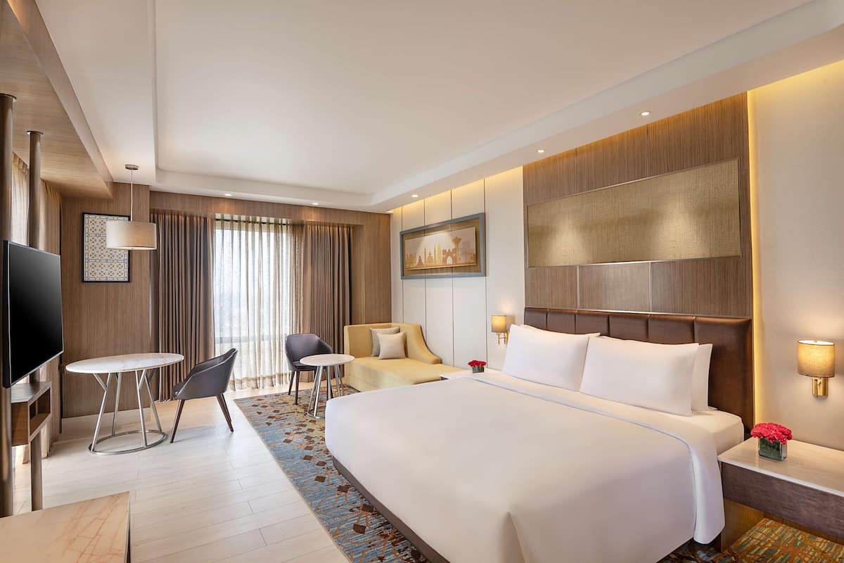 A hotel room with a large bed, a TV, a small table, and a sofa.