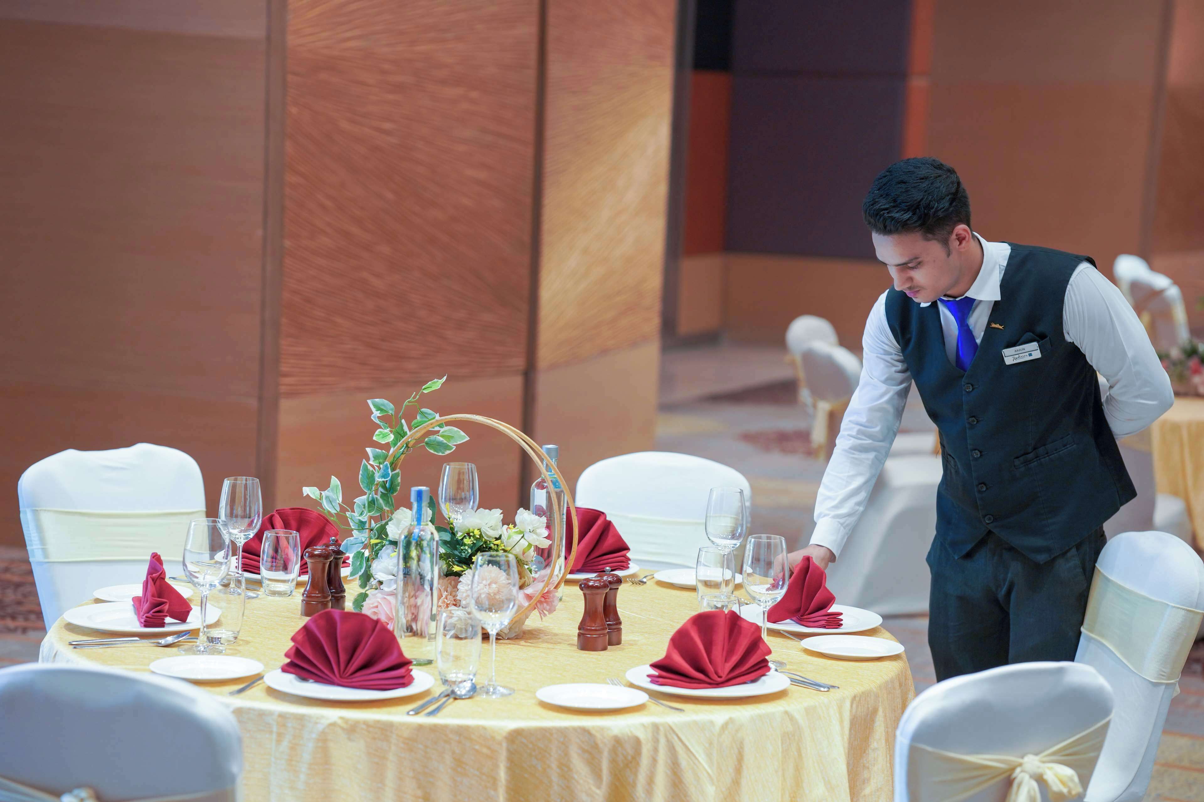 Una mesa de banquete dispuesta con sillas blancas, servilletas rojas y copas de vidrio transparente.