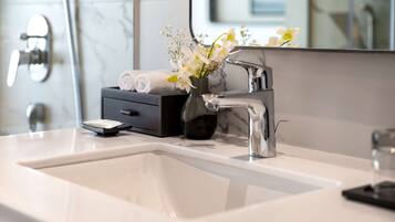 A modern bathroom with a white sink, chrome faucet, and a vase with white flowers.