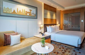 A hotel room with a large bed, a sofa, a small table with a plant, and a wall-mounted artwork depicting a cityscape. - Radisson Blu Hotel Amritsar (Amritsar)
