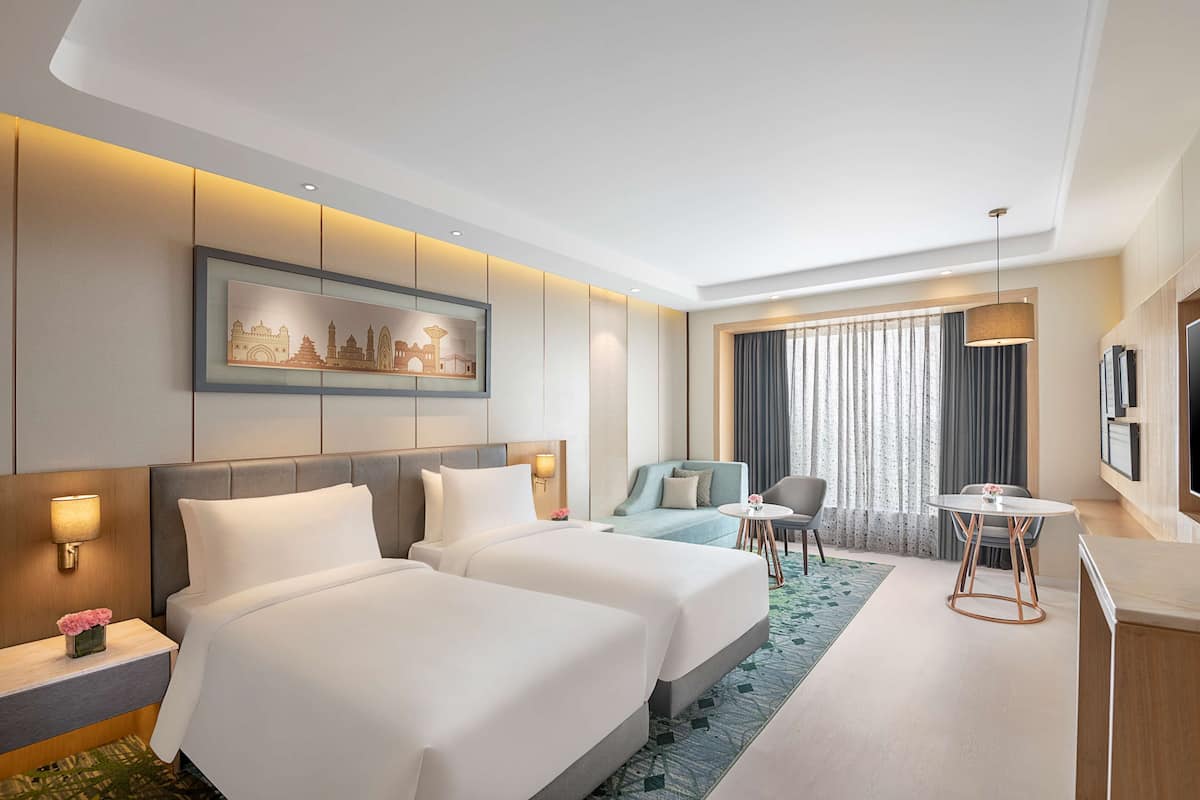 A hotel room with two beds, a sofa, a small table, and a TV.