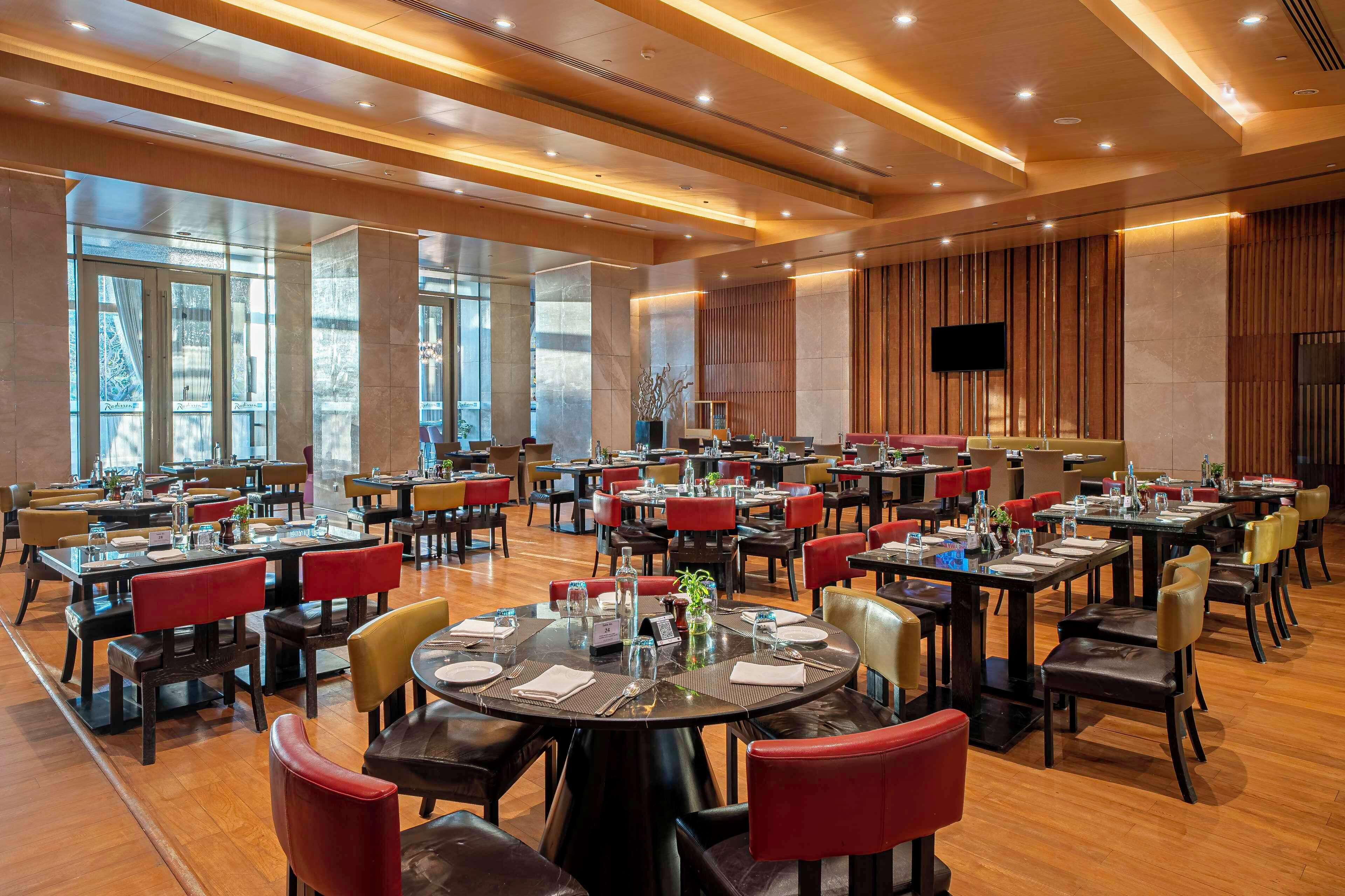A spacious dining area with multiple tables and chairs, large windows, and a modern ceiling design.