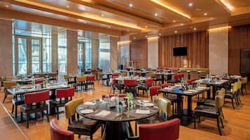 A spacious dining area with multiple tables and chairs, large windows, and a modern ceiling design.
