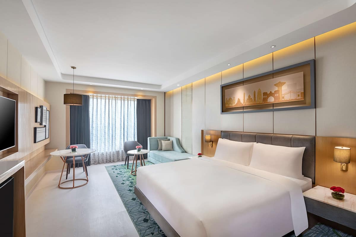 A modern hotel room with a large bed, a TV, a seating area with a table and chairs, and a cityscape artwork on the wall.
