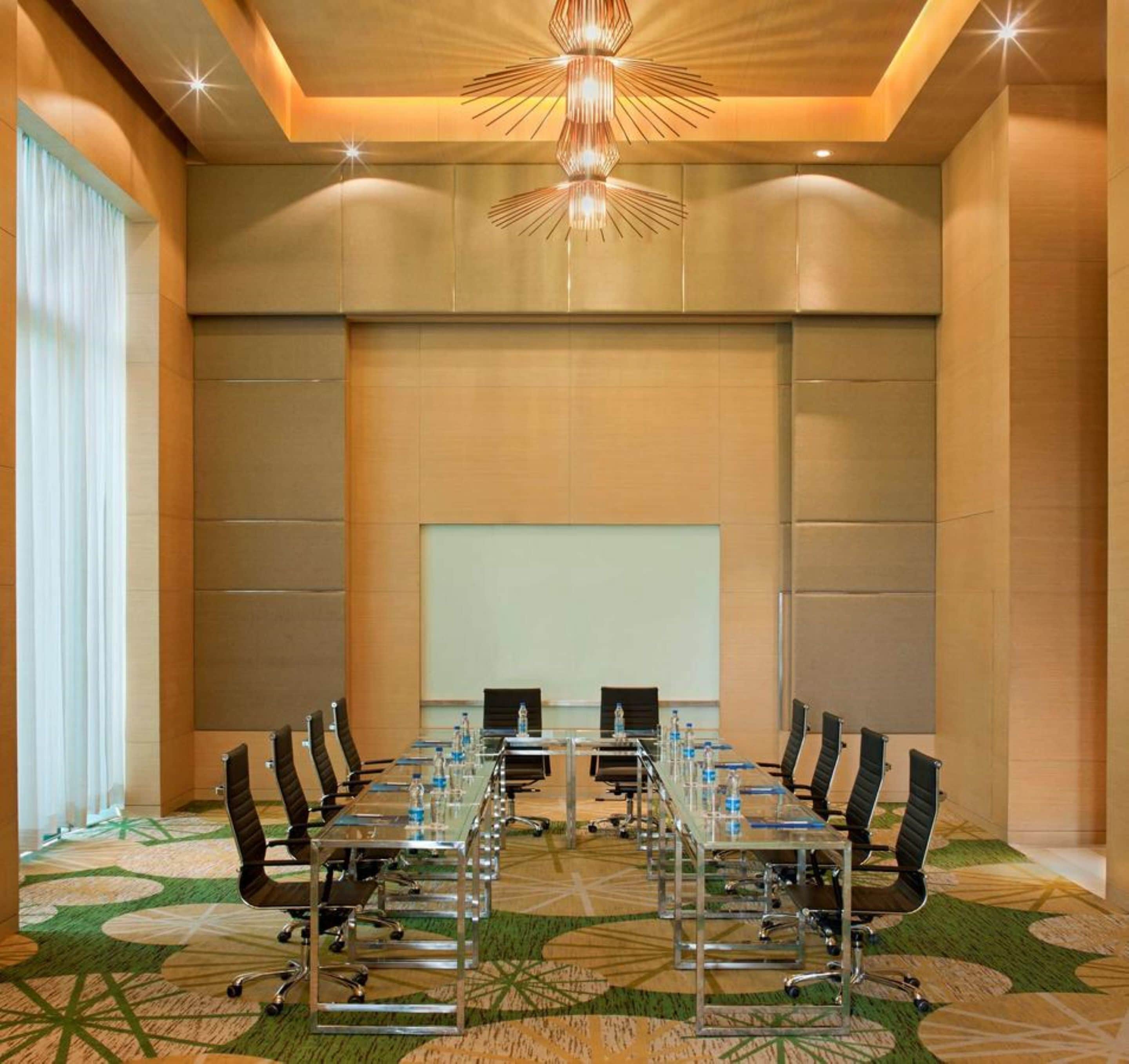 A conference room with a long table, chairs, a projector screen, and a carpeted floor.