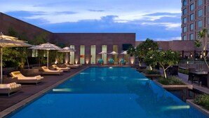 A swimming pool with lounge chairs and umbrellas, surrounded by a modern building with large windows. - Radisson Blu Hotel Amritsar (Amritsar)
