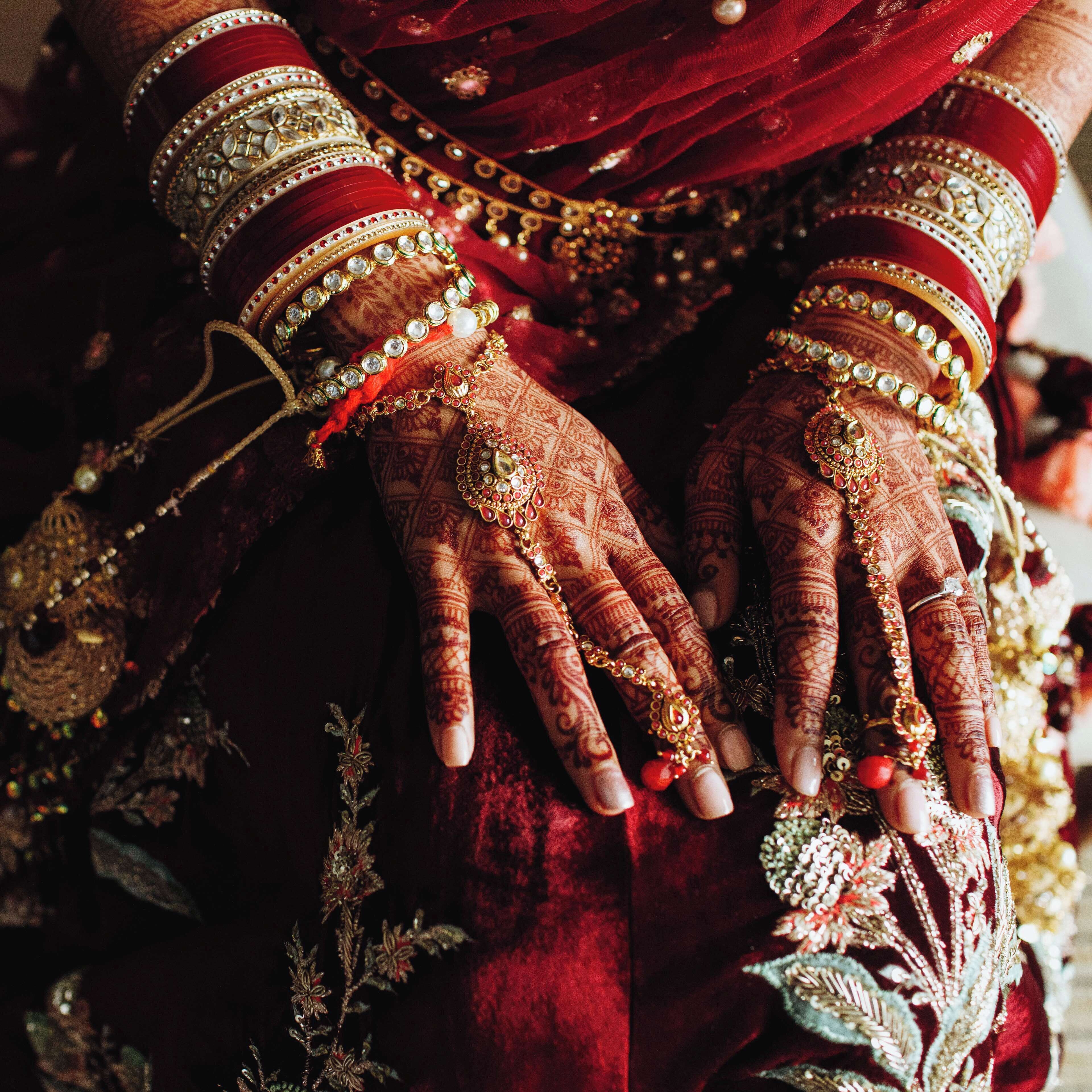 En närbild på händer som är utsmyckade med intrikata henna-mönster och smycken, vilket antyder ett kulturellt eller traditionellt sammanhang.