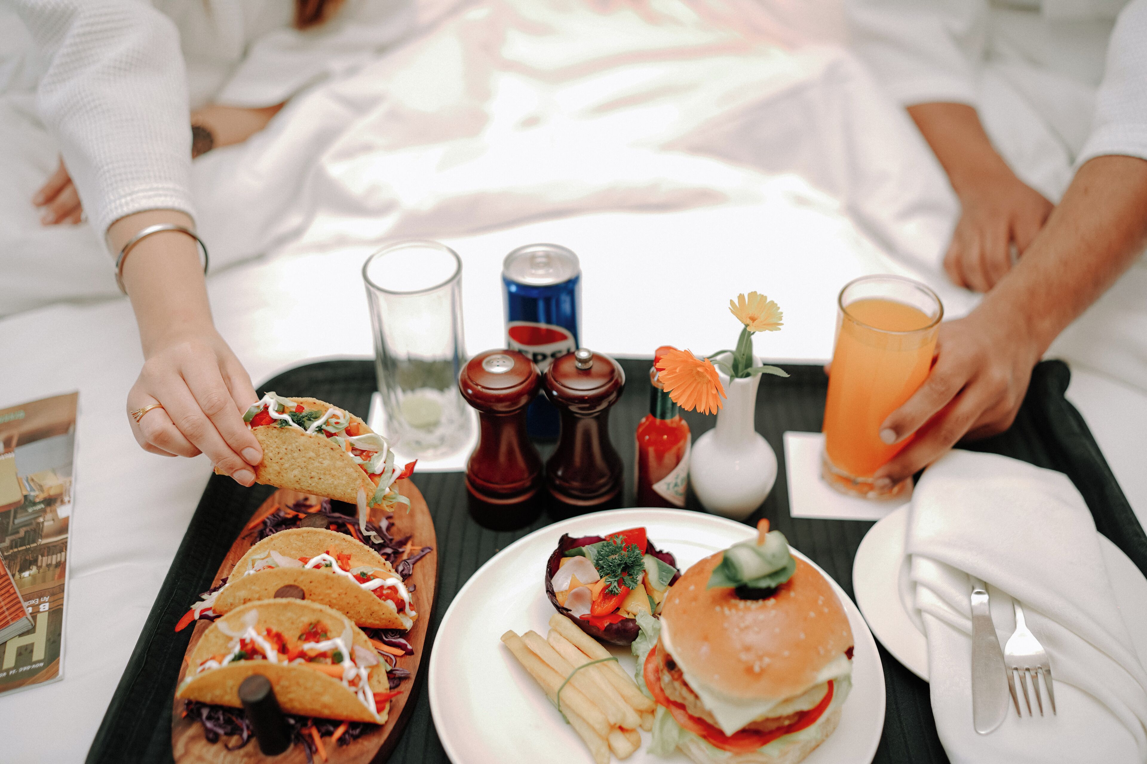 A tray with tacos, a burger, fries, and a glass of orange juice.