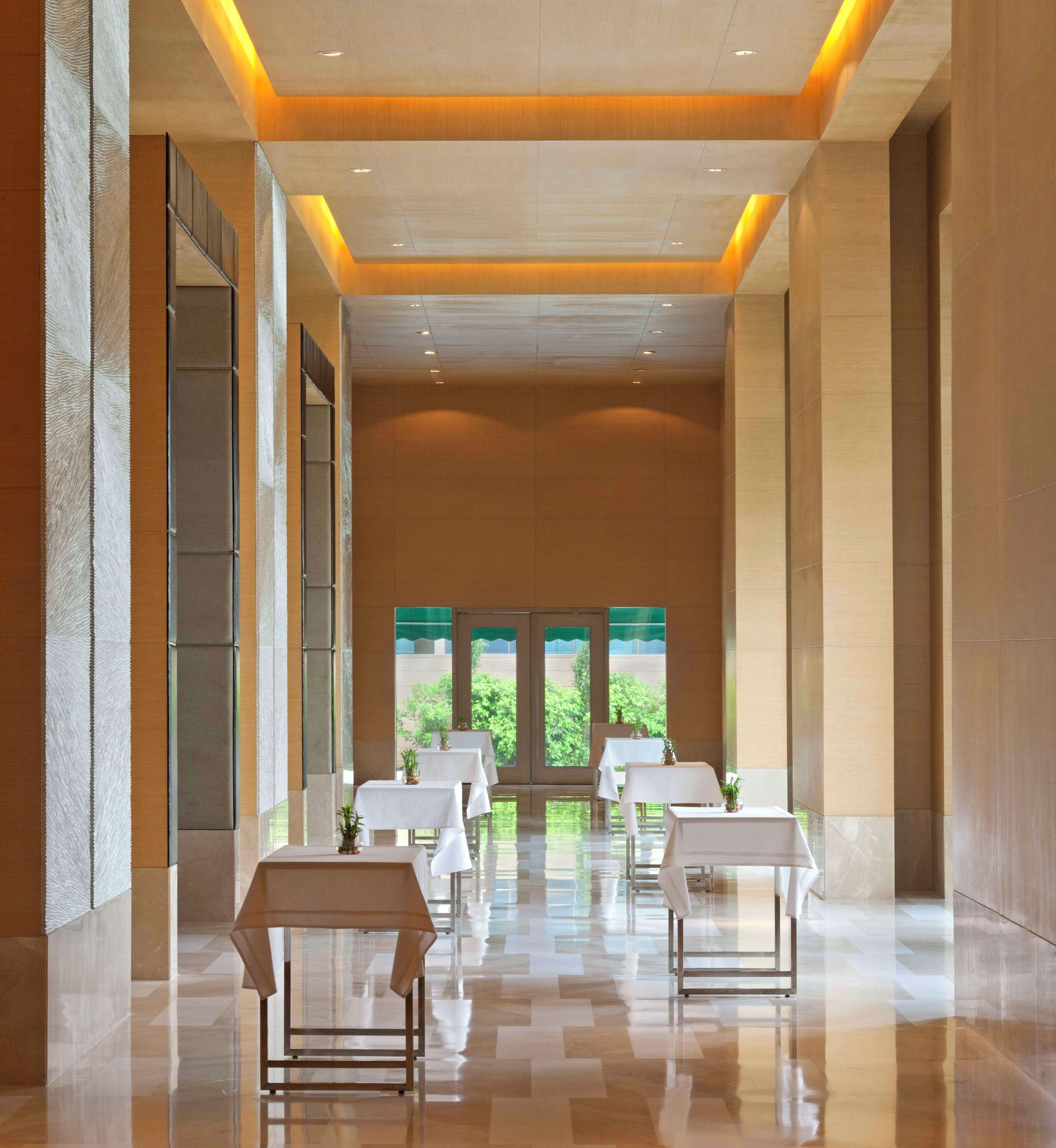 A spacious corridor with tables and chairs, large windows, and a view of greenery outside.