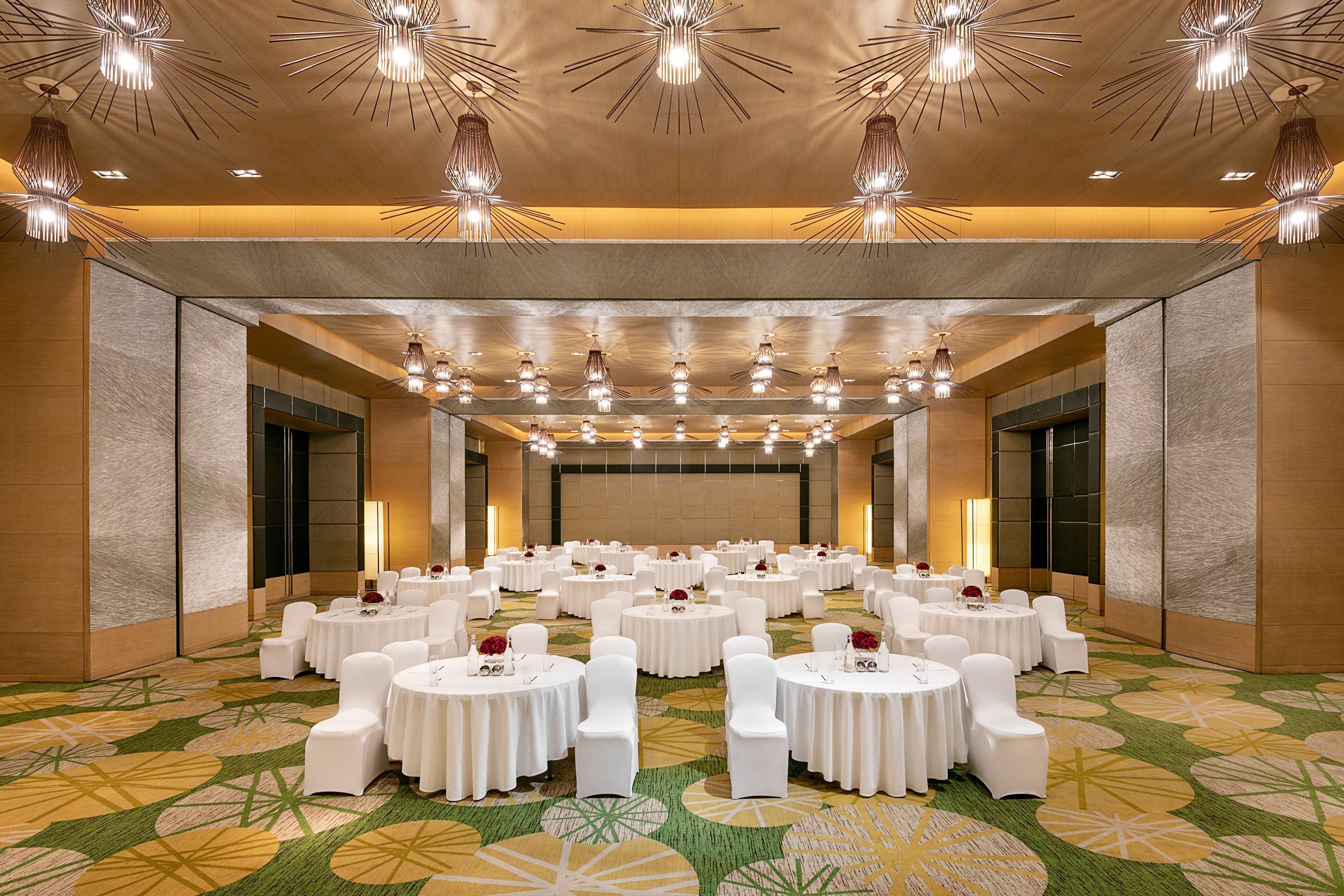 A large banquet hall with multiple round tables, white chairs, and overhead lighting fixtures.