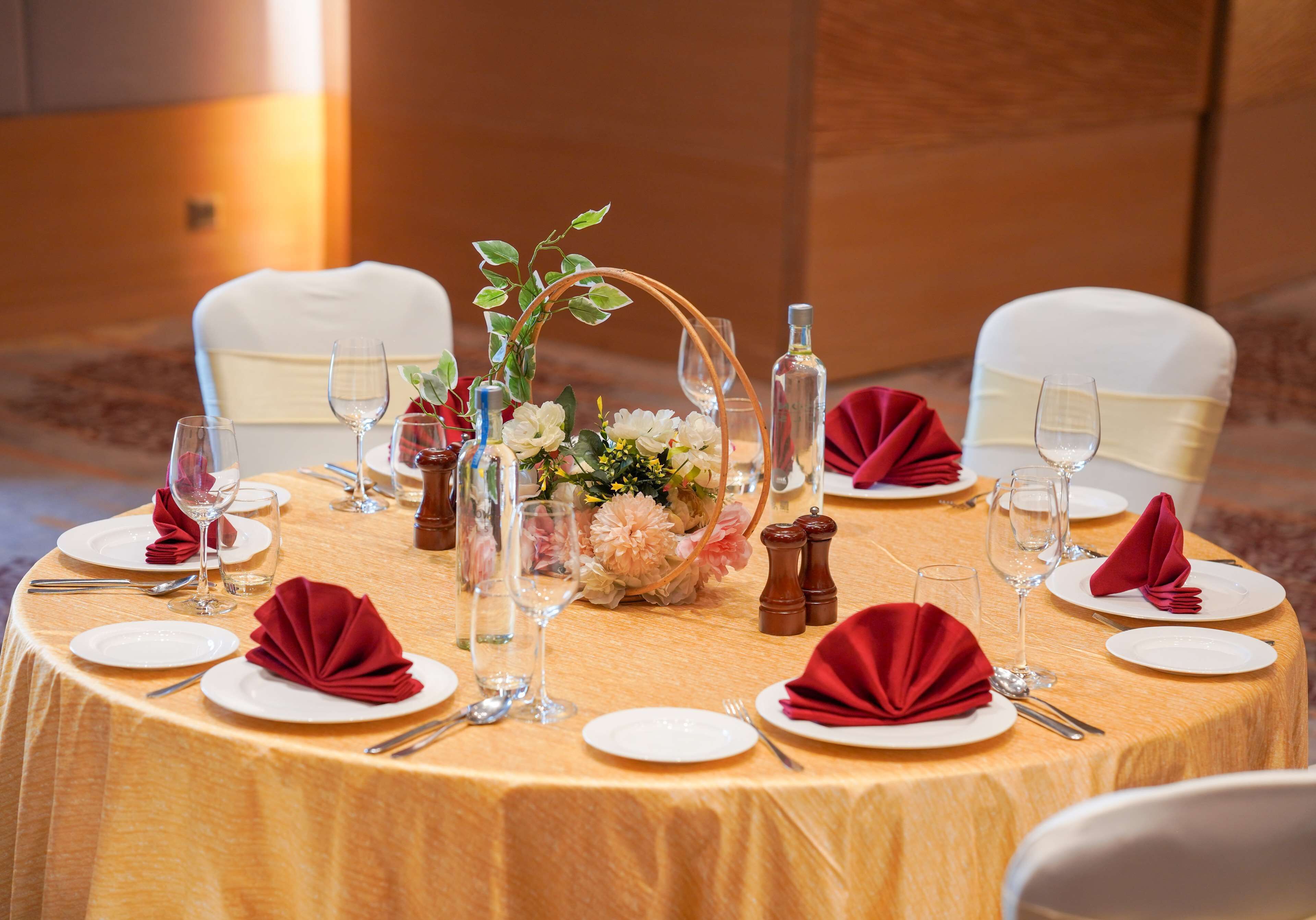 A round table set for a formal event with white plates, red napkins, and clear glassware.