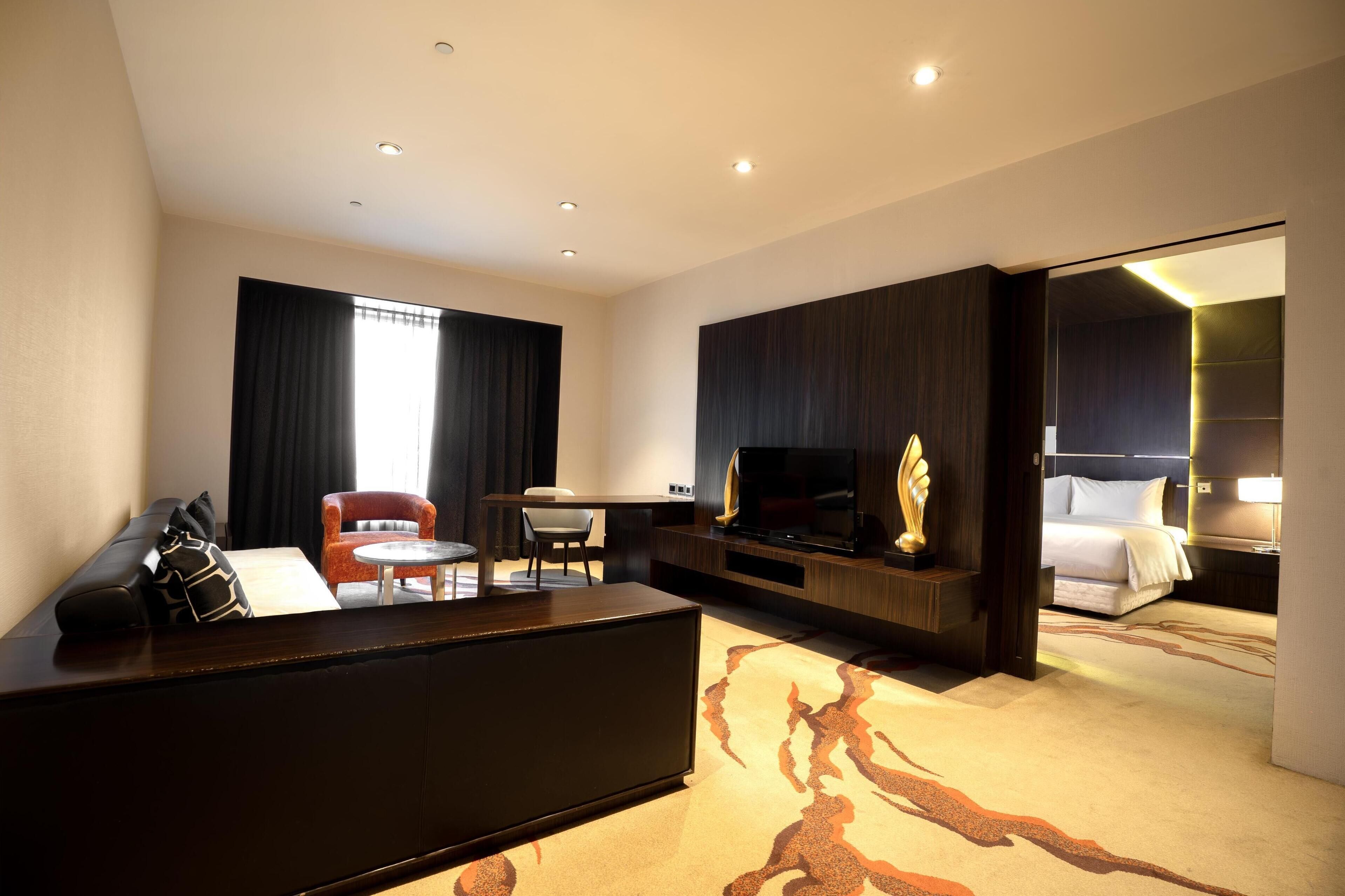 A modern hotel room with a sofa, a dining table, a TV, and a bed.