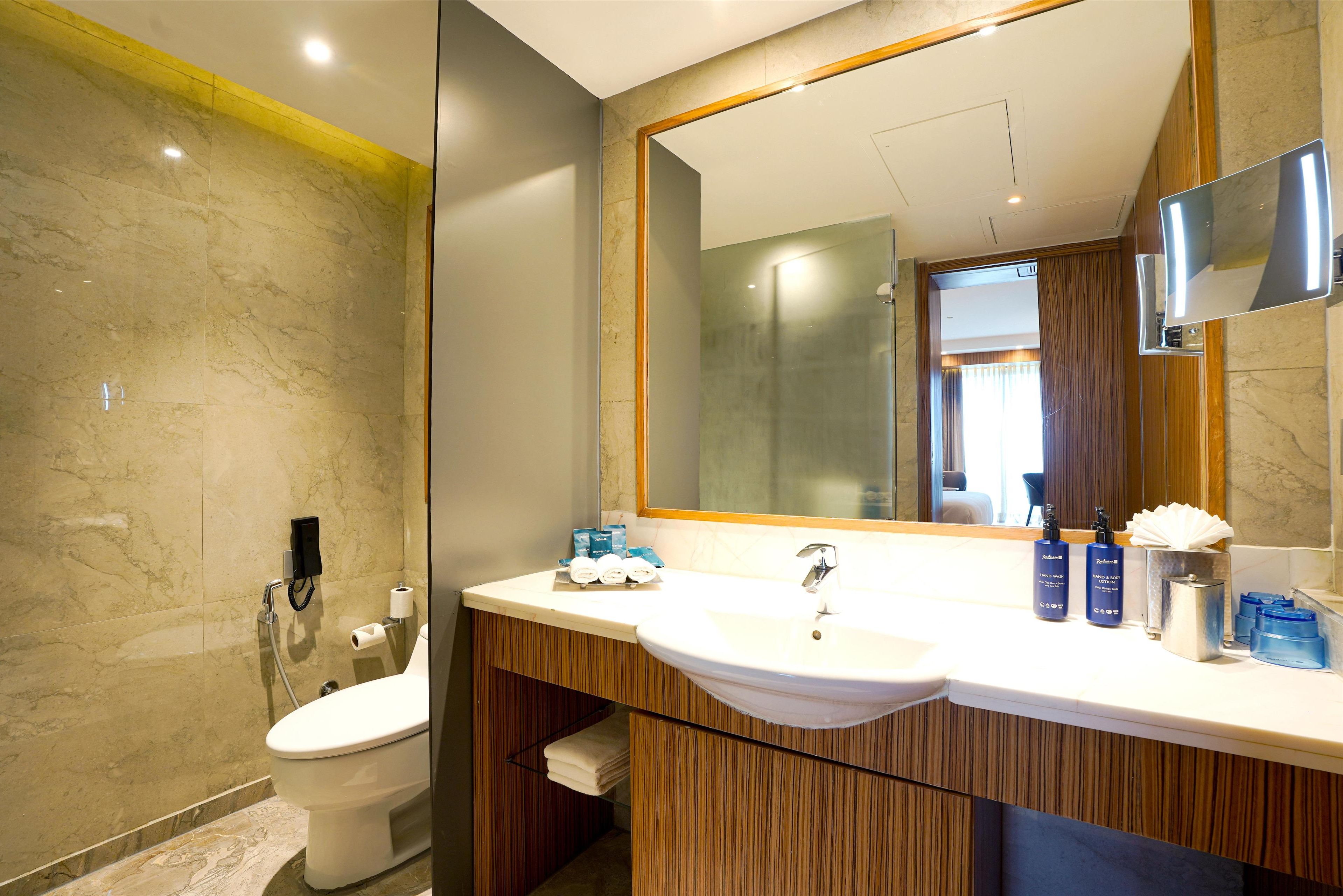A modern bathroom with a marble wall, a large mirror, and a wooden vanity.