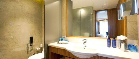 A modern bathroom with a marble wall, a large mirror, and a wooden vanity.