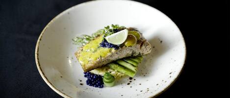 A plate with a piece of fish, green vegetables, and a slice of lime on a dark background.
