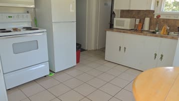 Una cocina con gabinetes blancos, estufa, refrigerador y microondas.