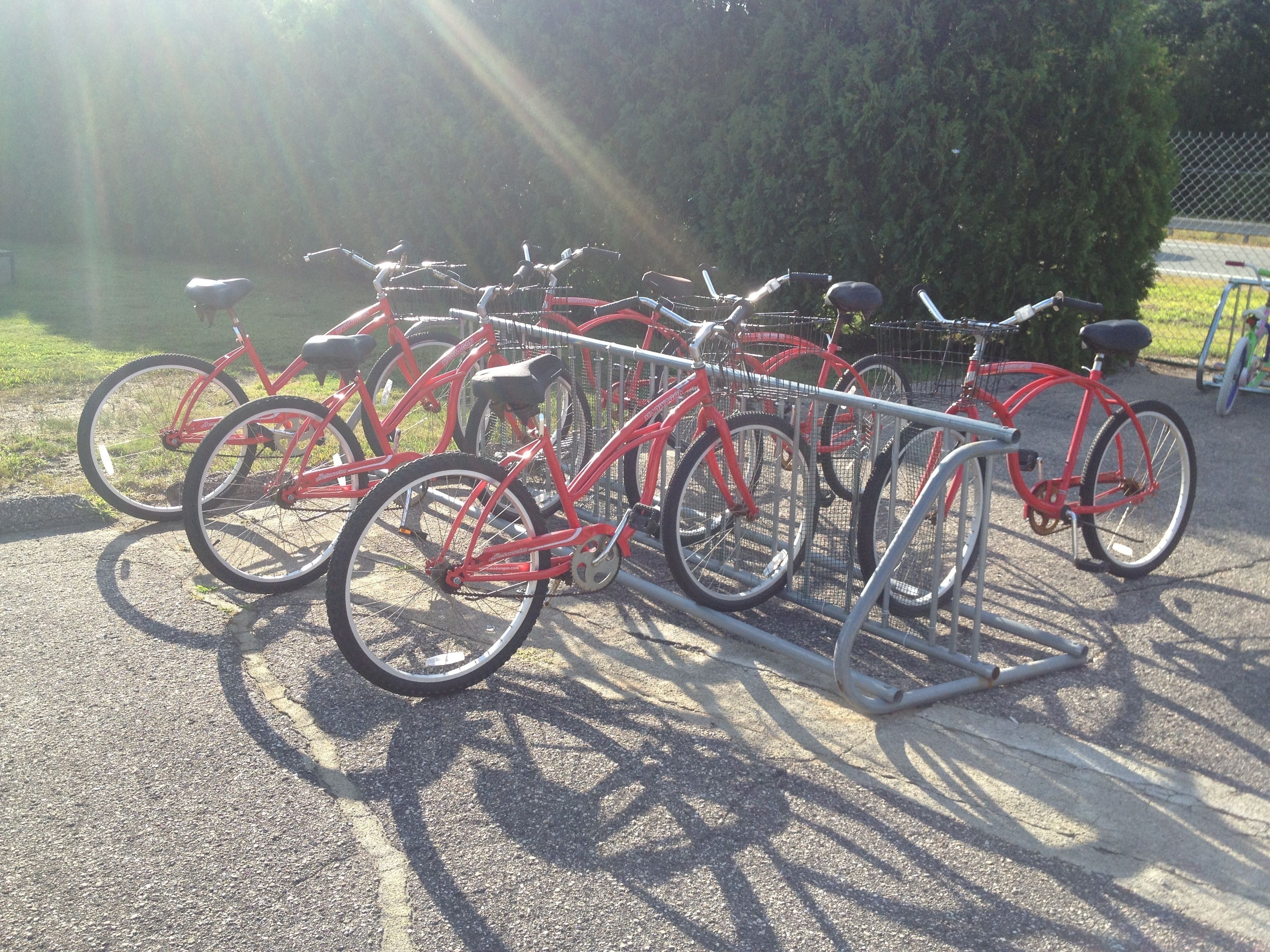 Une rangée de vélos rouges est garée sur une surface en béton, à côté d’un support métallique.
