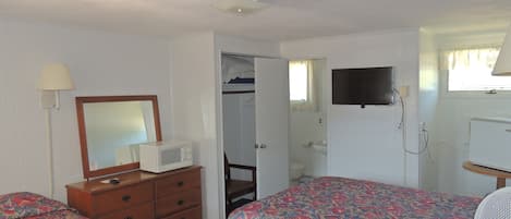 A room with two beds, a dresser, a mirror, a television, and a ceiling fan.