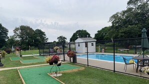 Un jardin avec une piscine, une pelouse artificielle verte et un petit abri de jardin.