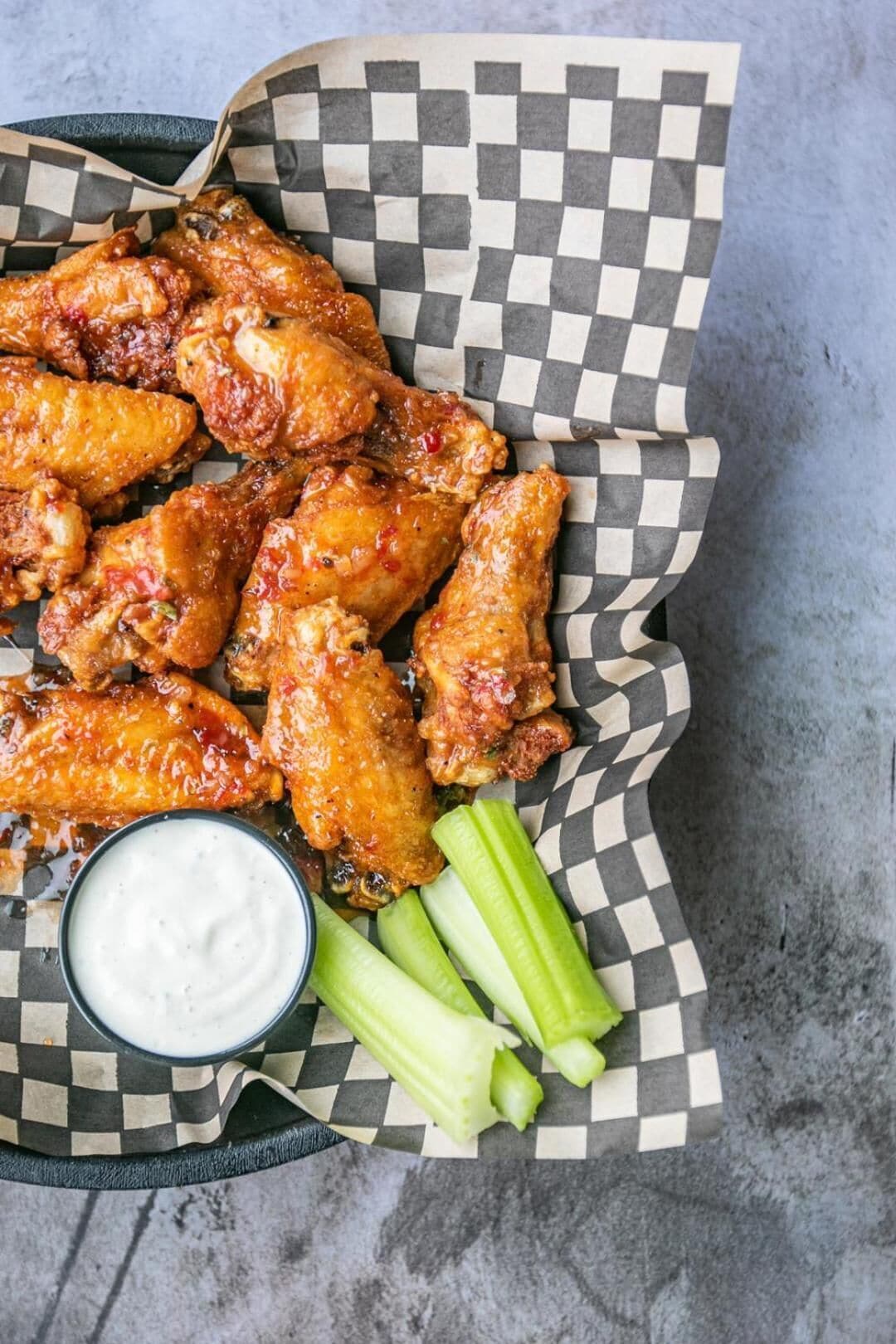 A tray of chicken wings with celery sticks and a dipping sauce.