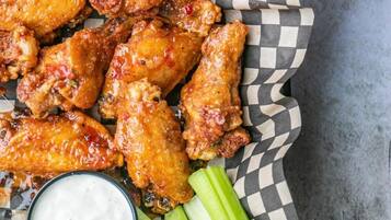 A tray of chicken wings with celery sticks and a dipping sauce.