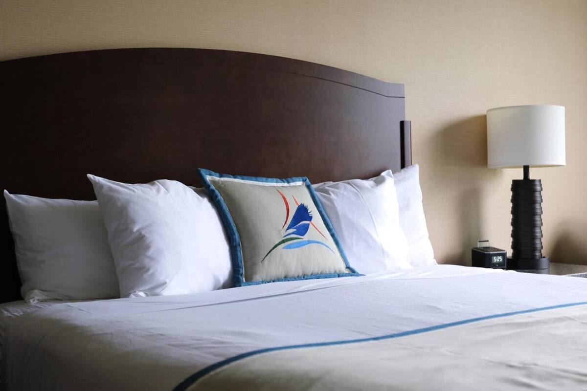 Una cama bien hecha con sábanas blancas y un cojín decorativo con diseño azul y rojo.