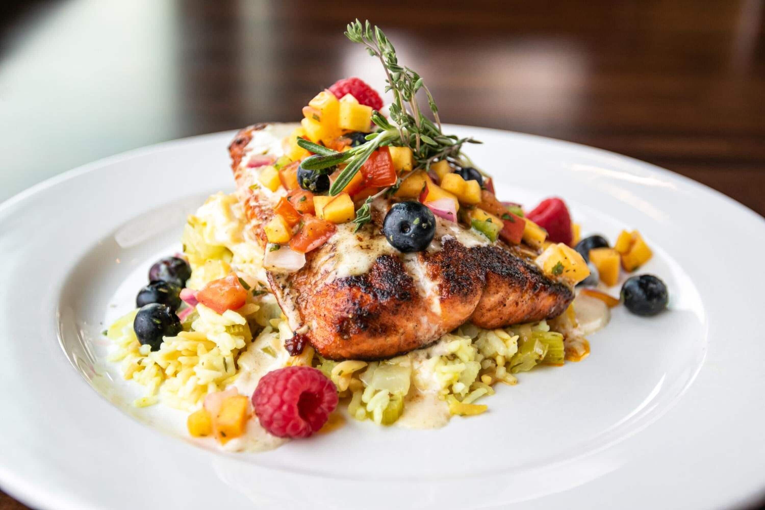 A plate of food with a grilled chicken breast, rice, and a variety of fruits and vegetables.