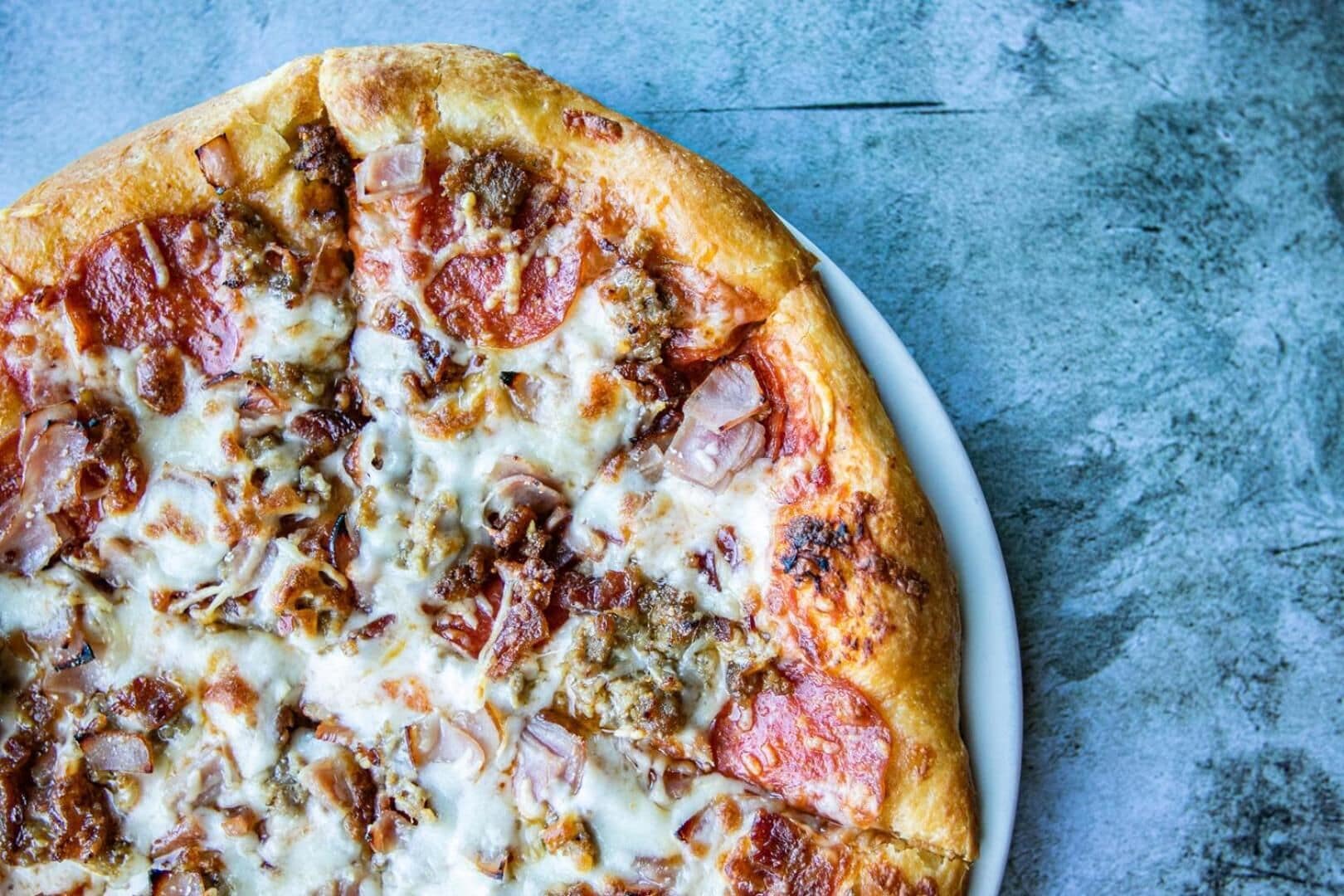 A pizza with pepperoni and onions on a white plate.