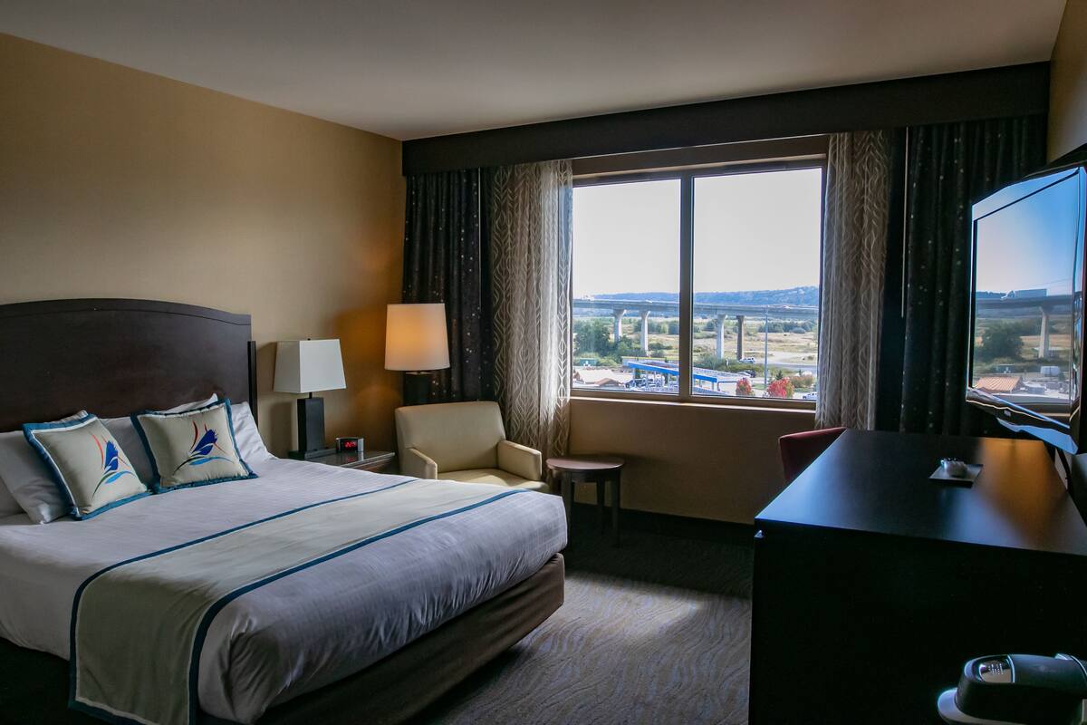 Habitación de hotel con una cama grande, un escritorio, una silla, un televisor y una ventana que ofrece vistas a un puente y un paisaje.