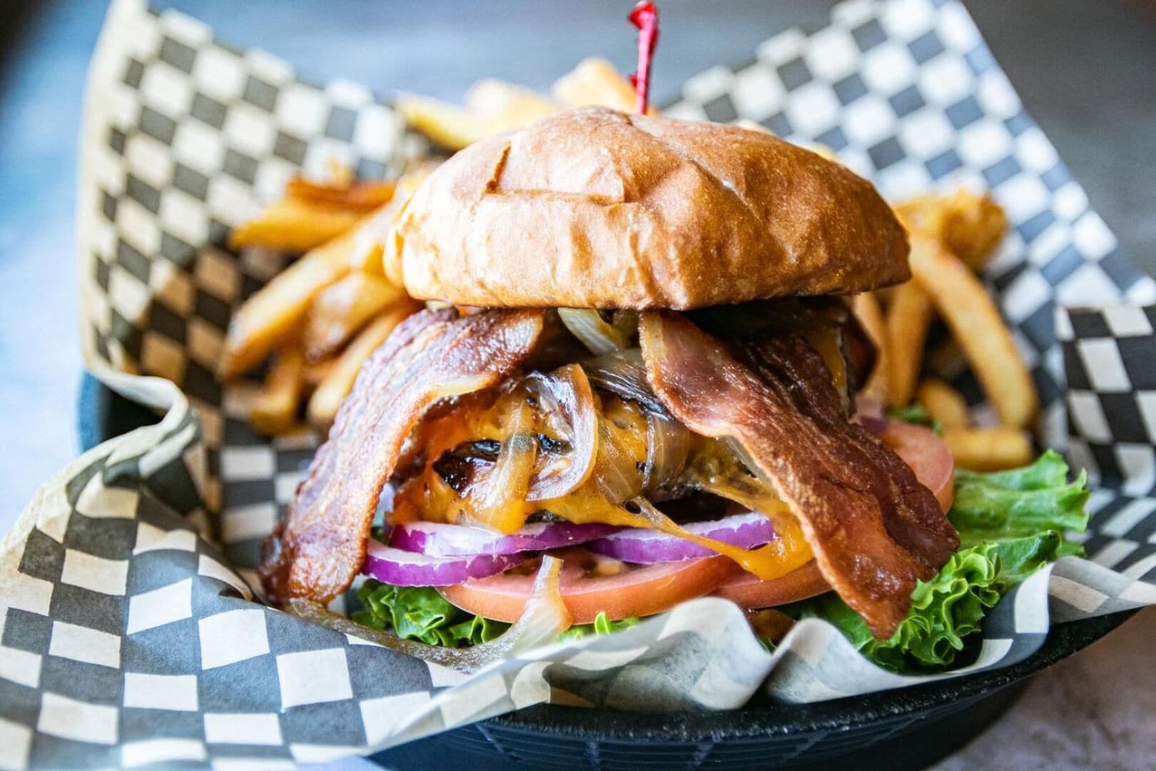 Hamburguesa con tocino, queso y lechuga, acompañada de papas fritas en un cesto de papel a cuadros.