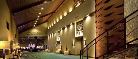 A spacious lobby with a high ceiling, a stone wall, and a staircase leading to an upper level.