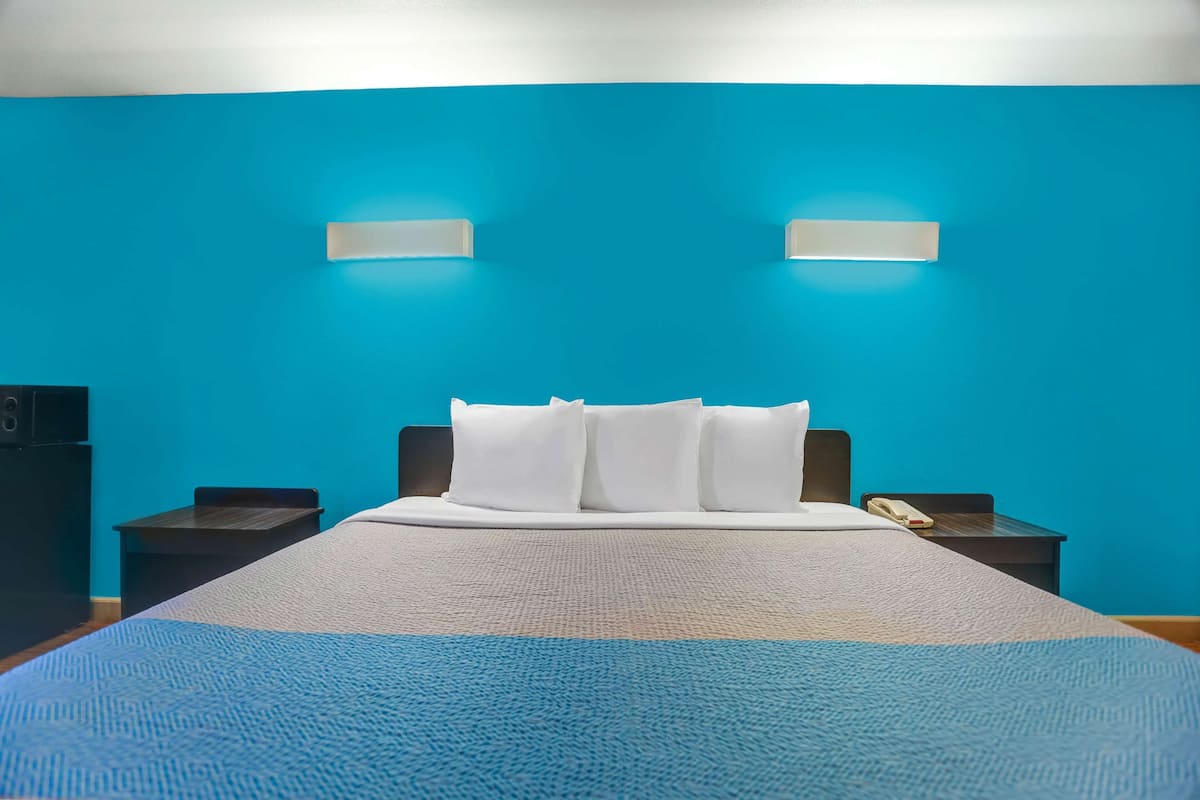 A hotel room with a large bed, two bedside tables, a nightstand, and two wall-mounted light fixtures.