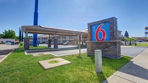 A motel with a large '6' sign, a covered parking area, and a well-maintained lawn.