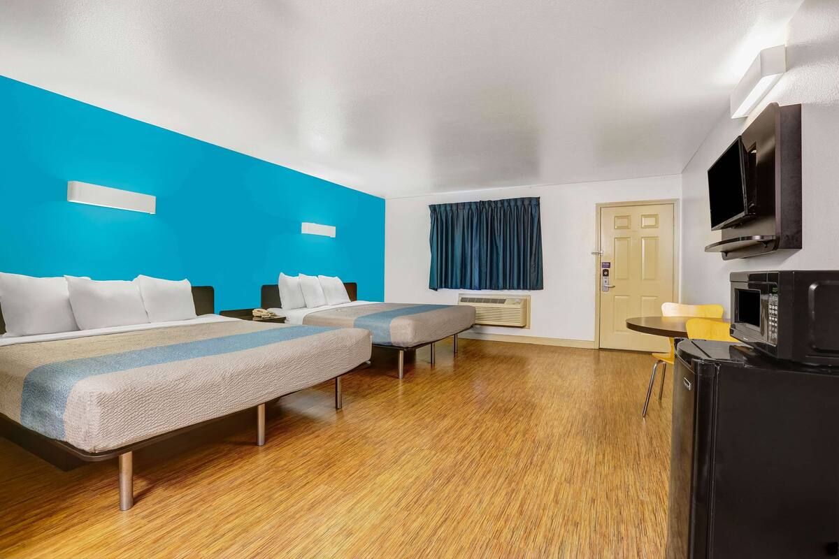 A hotel room with two beds, a TV, a microwave, and a small table.