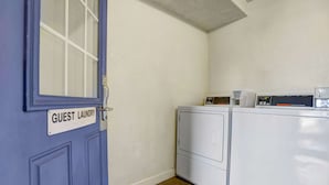 A laundry room with a blue door labeled "GUEST LAUNDRY," a stacked washer and dryer, and a control panel on the dryer.