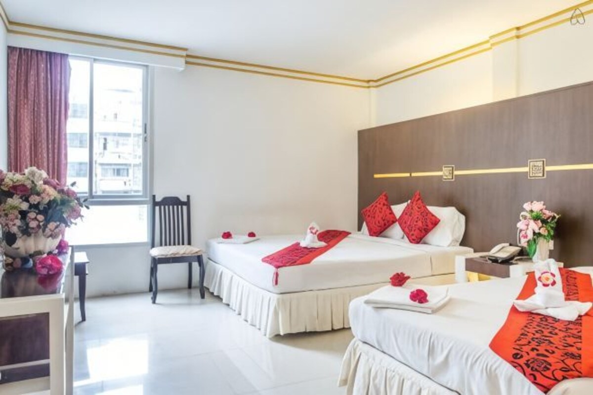 A hotel room with two beds, a desk, a chair, and a window.