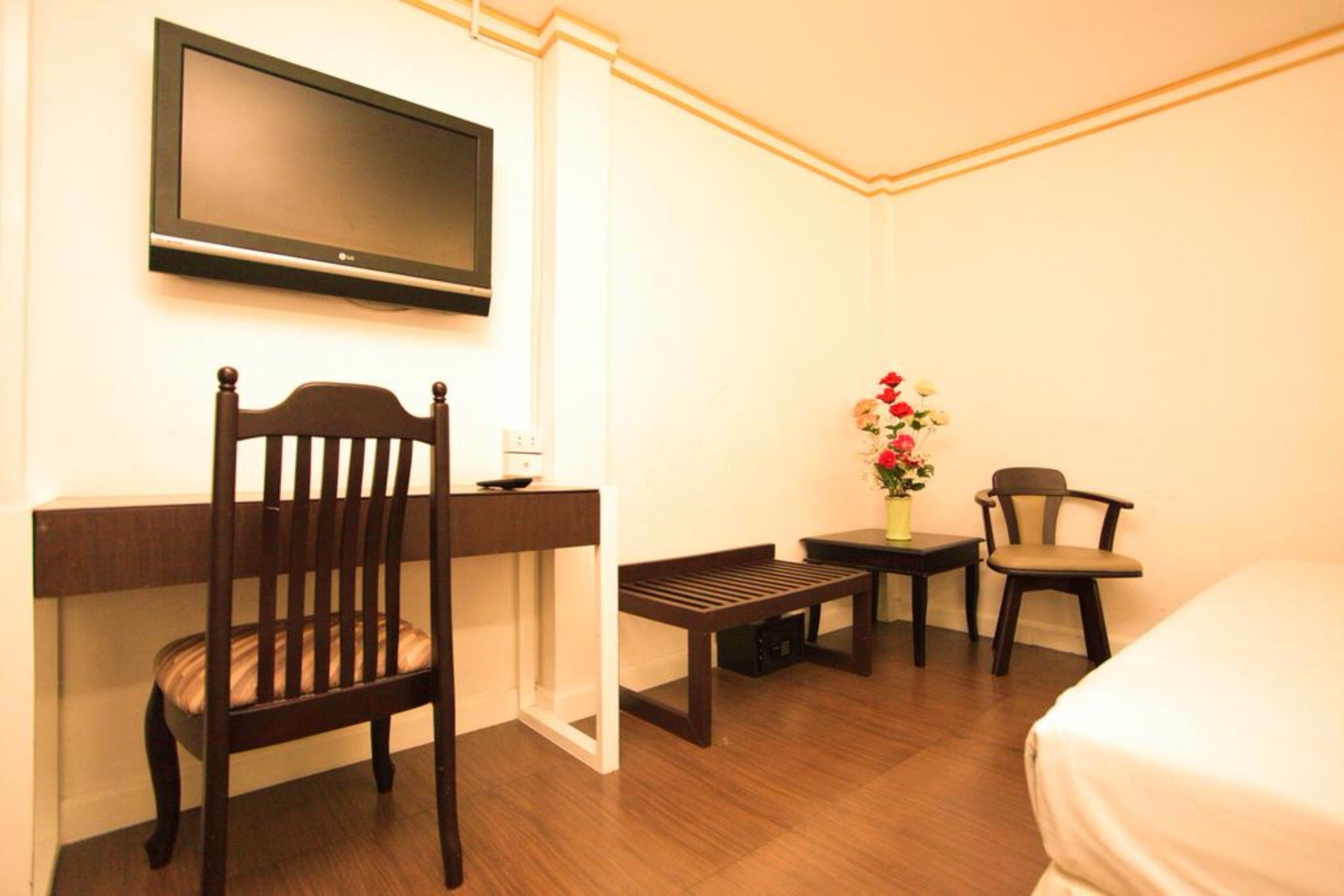 A hotel room with a wooden desk, a chair, a small table with a vase of flowers, and a bed.