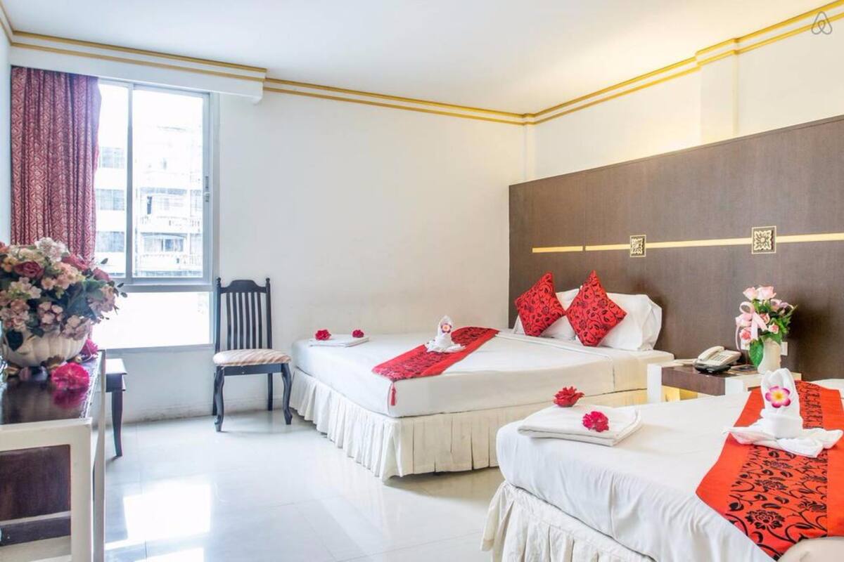 A hotel room with two beds, a desk, a chair, and a window with curtains.