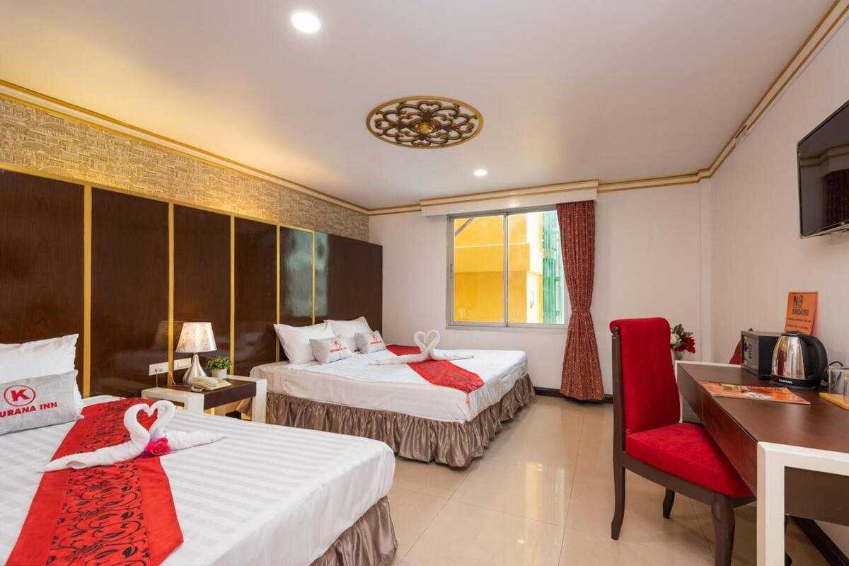 A hotel room with two beds, a desk, a chair, a TV, and a window with curtains.