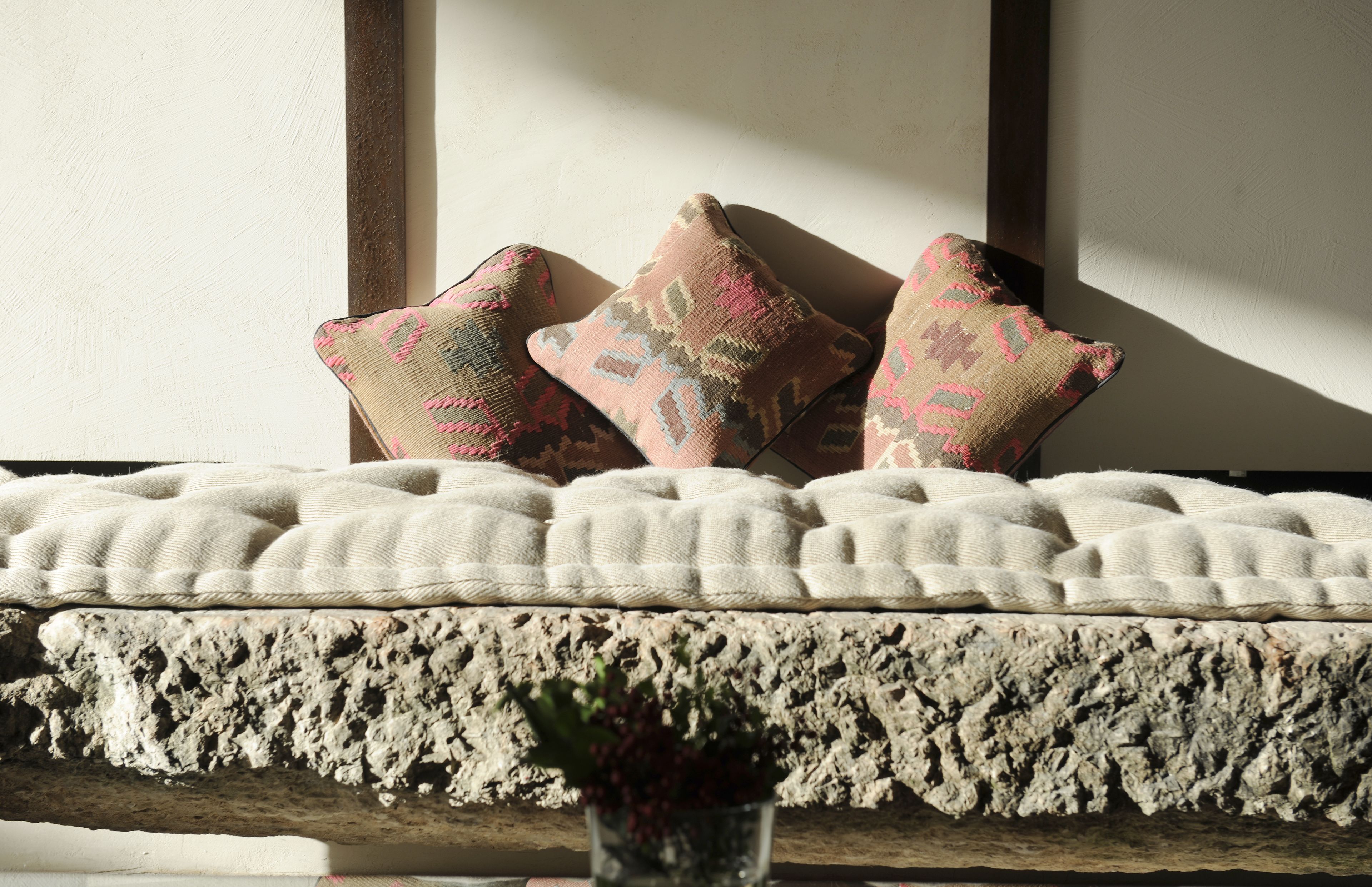 Ein strukturiertes Sofa mit drei gemusterten Kissen vor einer Wand mit Holzbalken.